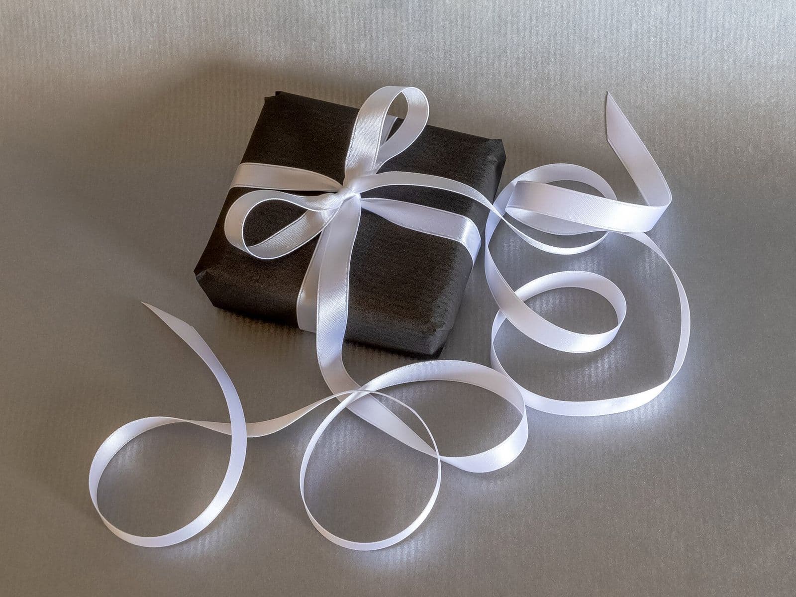 Gift wrapped in dark paper and tied with a white satin ribbon